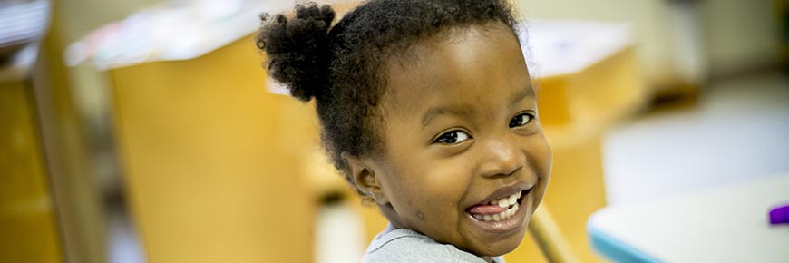 Girl smiles at the camera while playing in a classroom at the VCU Child Development Center.